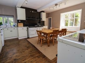 A kitchen with wooden floor white cabinets a wooden dining table with chairs and a large window at New Hall in Chirk