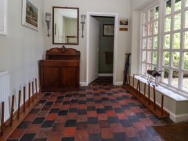 A hallway with checkered red and black tile floor wooden cabinet with mirror and sconces umbrella stands and window at New Hall in Chirk