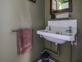 A bathroom sink with two taps wall mirror towel rail with a hanging towel and a trash bin below at New Hall in Chirk