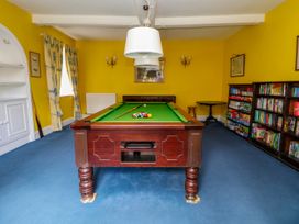 A room with a pool table in the center blue carpet yellow walls bookshelves and curtains at New Hall in Chirk