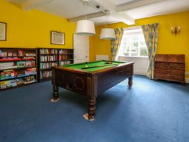 A game room with a pool table blue carpet yellow walls bookshelves filled with books and board games and a window with patterned curtains at New Hall in Chirk