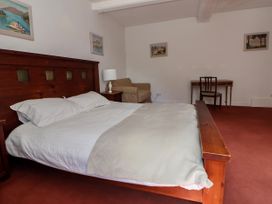 A bedroom with a wooden bed a bedside table with a lamp an armchair a desk with a chair and paintings on the walls at New Hall in Chirk