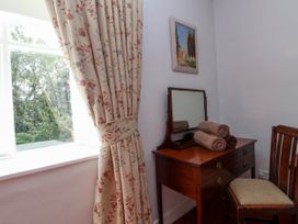 A wooden dressing table with a mirror and rolled towels next to a wooden chair and window with floral curtains at New Hall in Chirk