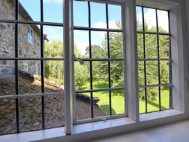 A view of a garden with trees and a stone building through a window with black grid frames at New Hall in Chirk
