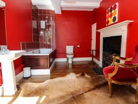 A bathroom with a bathtub sink toilet red walls wooden floor animal hide rug fireplace and a red chair at New Hall in Chirk