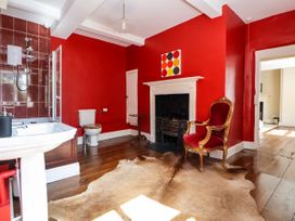 A bathroom with red walls a white bathtub white sink toilet a fireplace red armchair and a brown rug at New Hall in Chirk