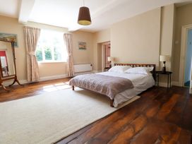 A bedroom with a wooden bed frame bedside tables lamps a large window with curtains a full length mirror and wooden floors at New Hall in Chirk