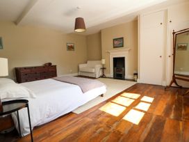 A bedroom with a bed a wooden dresser a white armchair a fireplace and a large mirror at New Hall in Chirk