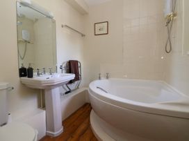 A bathroom with a corner bathtub wooden floor a pedestal sink and a toilet at New Hall in Chirk