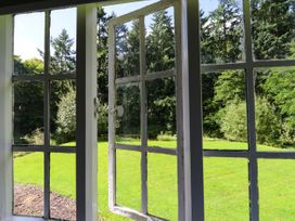 A view through a white framed window opening to a garden with green grass and trees at New Hall in Chirk