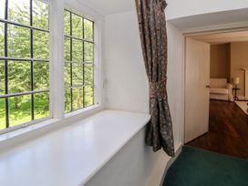 A window with leaded glass panels and patterned curtain next to a doorway showing a room with a white armchair on wooden floor at New Hall in Chirk