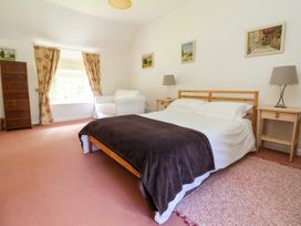 A bedroom with a double bed white armchair framed paintings and wooden furniture at New Hall in Chirk