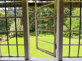 A view of a green lawn and trees through a partially open window with metal grid panes at New Hall in Chirk