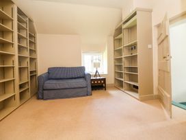 A room with empty beige bookshelves a blue checkered sofa a wooden side table with a lamp and a small window at New Hall in Chirk