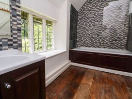 A bathroom with a wooden floor a bathtub with a tiled wall and a window with multiple panes at New Hall in Chirk