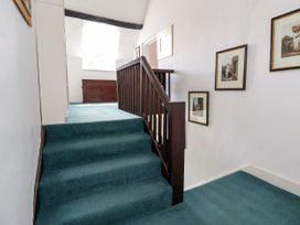 A carpeted staircase with wooden railing leading to a landing with framed pictures on the wall at New Hall in Chirk