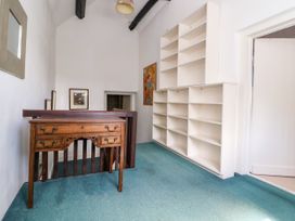 A hallway with a wooden desk white shelves framed pictures on the wall and teal carpet at New Hall in Chirk