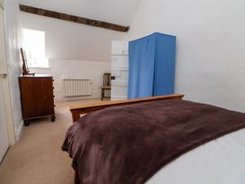 A bedroom with a bed covered by a brown blanket a blue fabric wardrobe a wooden dresser with a mirror and a chair near a window at New Hall in Chirk