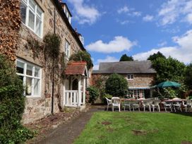 An outdoor garden area with white and metal chairs and tables under umbrellas next to a stone building at New Hall in Chirk