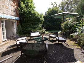 An outdoor patio with chairs a table umbrella and greenery at New Hall in Chirk