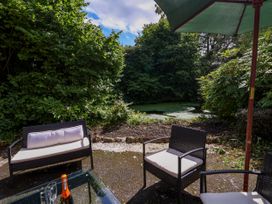 An outdoor seating area with a table glassware a bottle and chairs near trees and a small pond at New Hall in Chirk