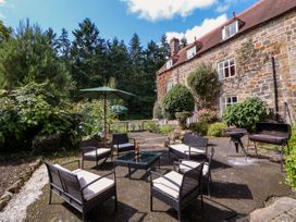 An outdoor patio with wicker chairs and cushions around a glass table a stone house and trees in the background at New Hall in Chirk