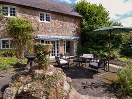 An outdoor patio area with black chairs and a table under a green umbrella beside a stone house with white windows at New Hall in Chirk