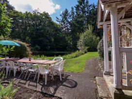 An outdoor patio with a wooden table and mixed white plastic and metal chairs near a grassy area and trees at New Hall in Chirk