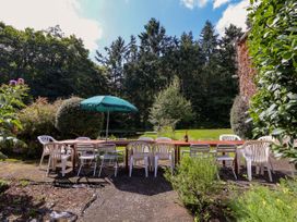 An outdoor patio area with a long wooden table surrounded by plastic and metal chairs under a green umbrella at New Hall in Chirk