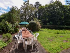 An outdoor dining area with white plastic chairs and wooden tables under a green umbrella in a garden with trees and grass at New Hall in Chirk