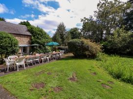 A long outdoor dining table with chairs and umbrellas in a garden next to a stone building at New Hall in Chirk