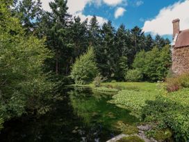 A pond with surrounding trees and greenery next to a building with a chimney at New Hall in Chirk