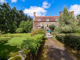 A stone house with a red tiled roof and garden furniture outside surrounded by trees and vegetation at New Hall in Chirk