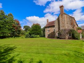 A stone house with chimneys next to a large green lawn and trees at New Hall in Chirk
