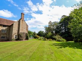 A stone house with a chimney next to a lawn and trees under a blue sky at New Hall in Chirk