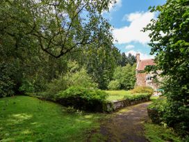 A garden lawn with trees and a stone house with a tiled roof at New Hall in Chirk