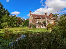 A stone house with multiple chimneys by a pond surrounded by grass and trees at New Hall in Chirk