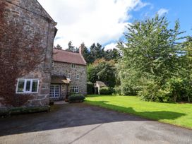 A stone house with multiple windows and a pitched roof beside a paved driveway and a grassy yard with trees at New Hall in Chirk