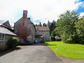 A stone house with multiple windows and a chimney next to a driveway and green lawn with trees at New Hall in Chirk