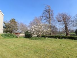 A garden with a grassy lawn several trees and a flowering tree near a building at Hen Ficerdy Abererch near Pwllheli