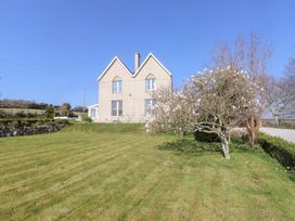A house with a lawn and flowering tree under a blue sky at Hen Ficerdy in Abererch near Pwllheli