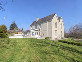 A large two-story house with a pitched roof and patio surrounded by a lawn at Hen Ficerdy in Abererch near Pwllheli