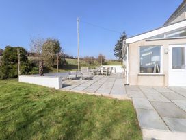 A patio with outdoor chairs and a table next to a house with lawn and trees at Hen Ficerdy Abererch near Pwllheli
