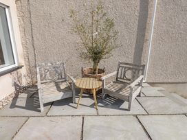 Two wooden chairs with a small round wooden table and a potted plant on a stone patio outside a building at Hen Ficerdy Abererch near Pwllheli