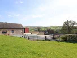 A building next to a field with a fence and road at The Granary in Llangyniew near Llanfair Caereinion
