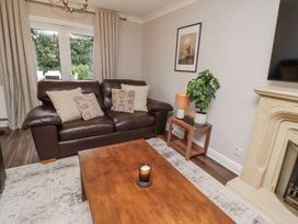 A living room with a brown leather sofa and cushions a wooden coffee table with a candle a small side table with a lamp and plant a fireplace and a wall-mounted TV at Sparrow House in Alnwick
