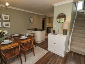A dining area with a wooden table set for six and a small cabinet with a lamp next to carpeted stairs at Sparrow House in Alnwick