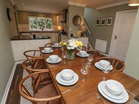 A dining area with a wooden table set with white dishes and glassware and a kitchen with counters and a window at Sparrow House in Alnwick