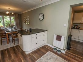 A dining area with a wooden table set with dishes and glasses next to a kitchen island with drawers and a wall clock at Sparrow House in Alnwick