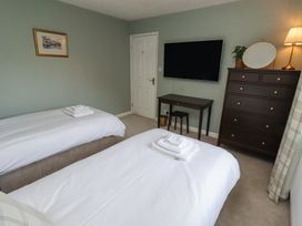 A bedroom with two beds white bedding a chest of drawers a wall mounted tv and a small desk at Sparrow House in Alnwick